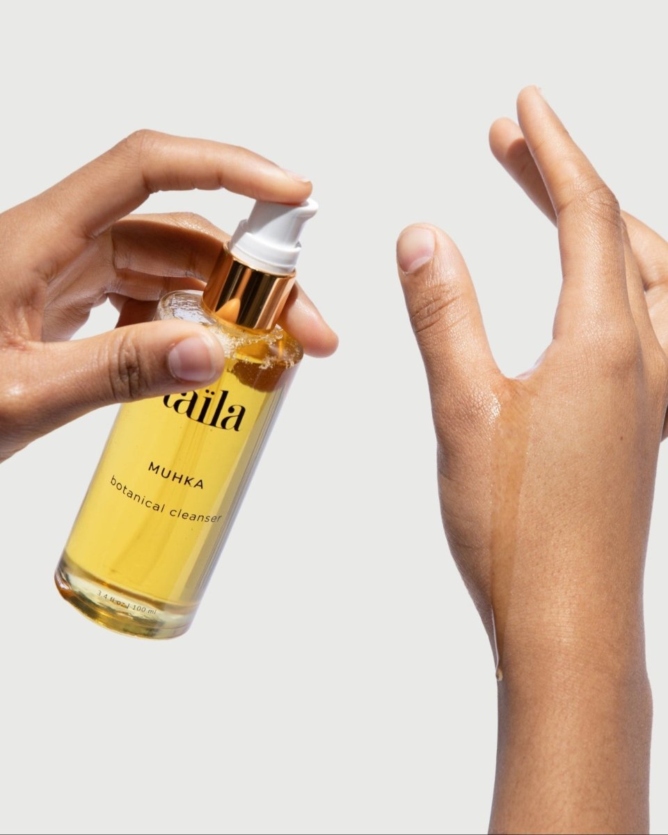 A hand gently holding the taïla MUHKA Botanical Oil Cleanser bottle against a clean, minimalist white background.