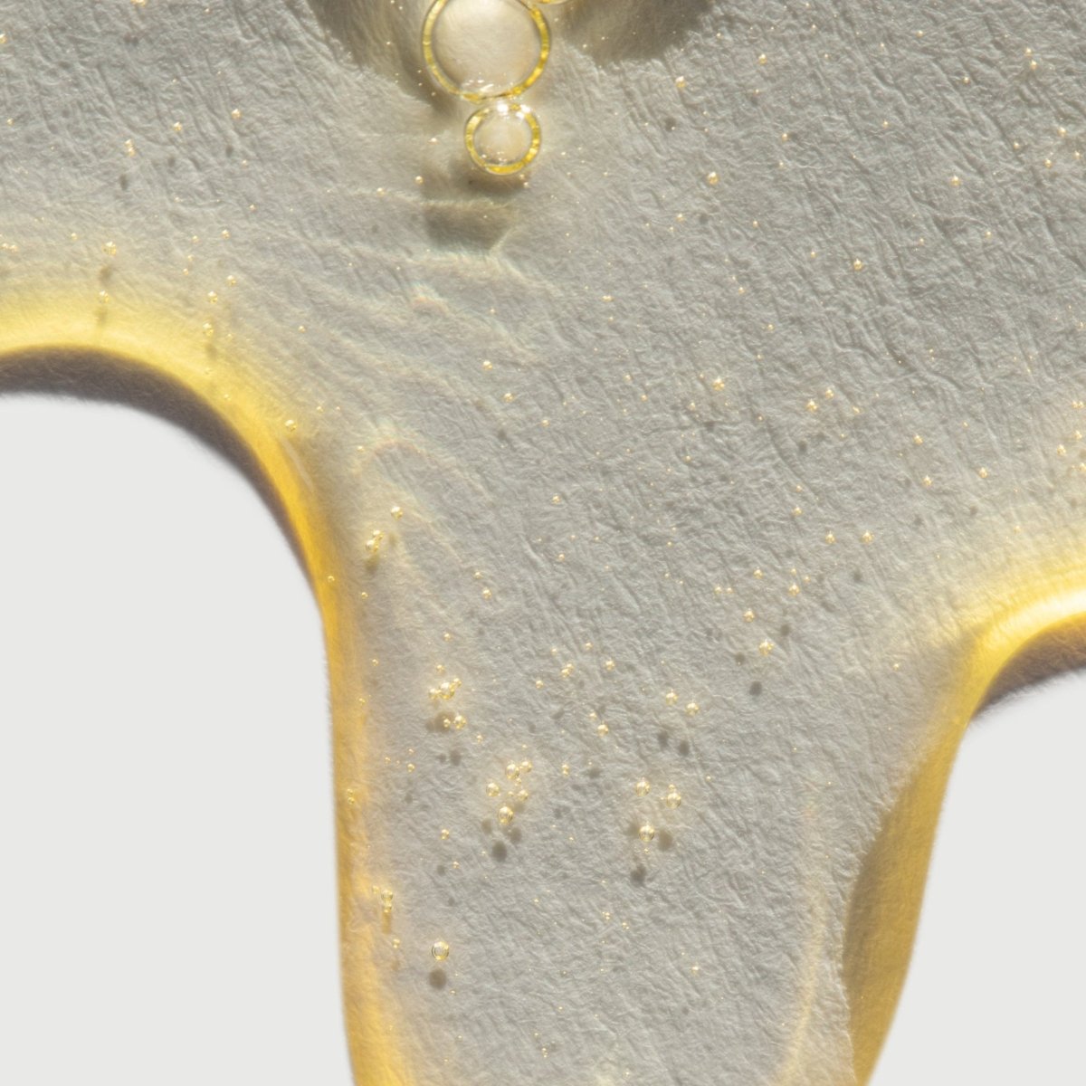 A close-up of the taïla MUHKA Botanical Cleanser texture emulsifying from a rich oil into a smooth, white milky lotion.