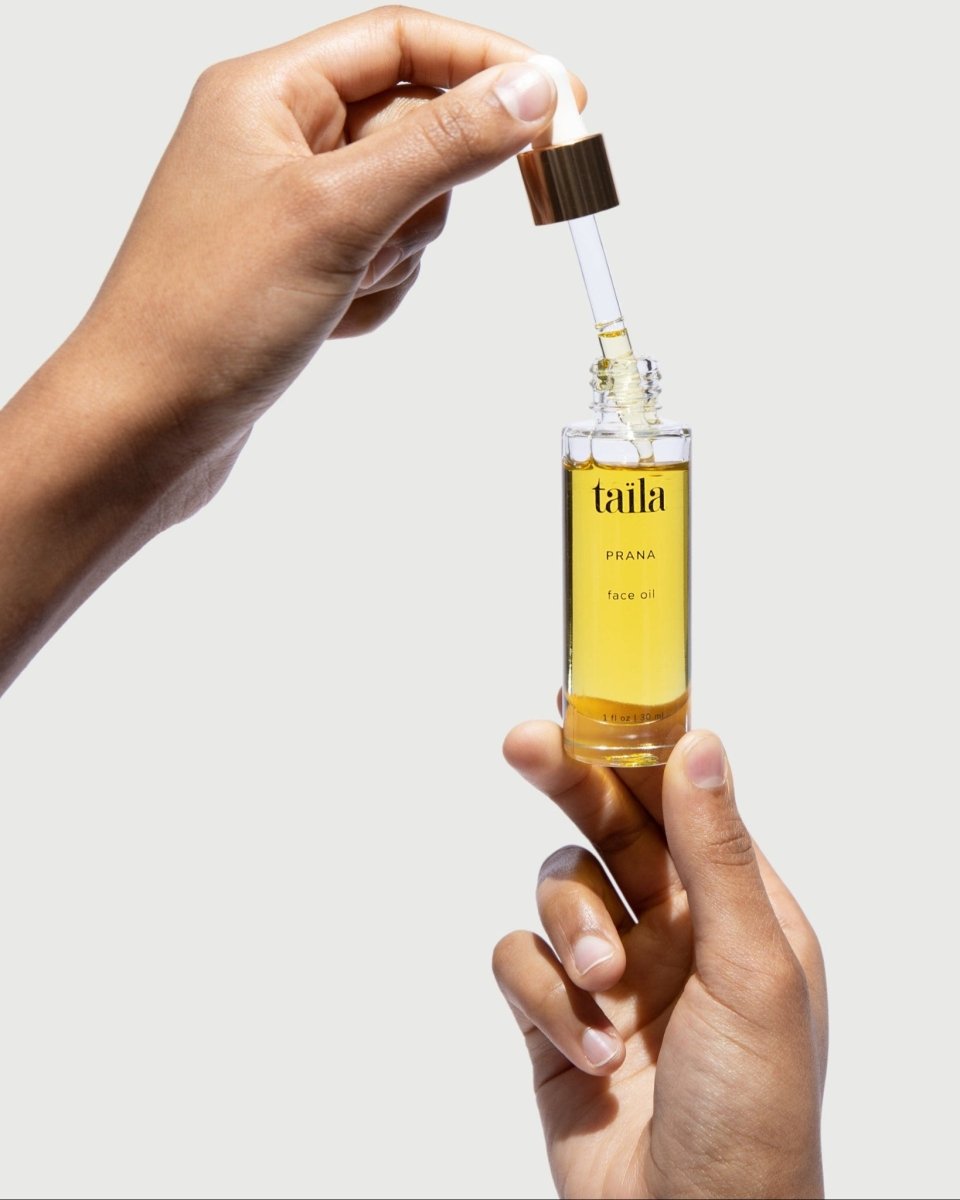A hand gently holding the taïla PRANA Face Oil bottle against a clean, minimalist white background.