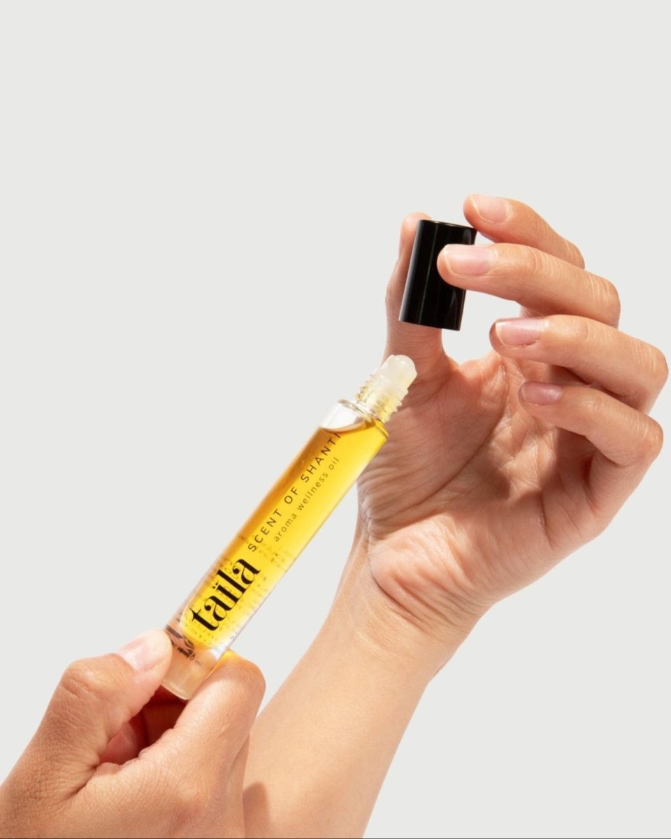 A hand gently holding the taïla Scent of Shanti Aroma Wellness Oil bottle against a minimalist white background.