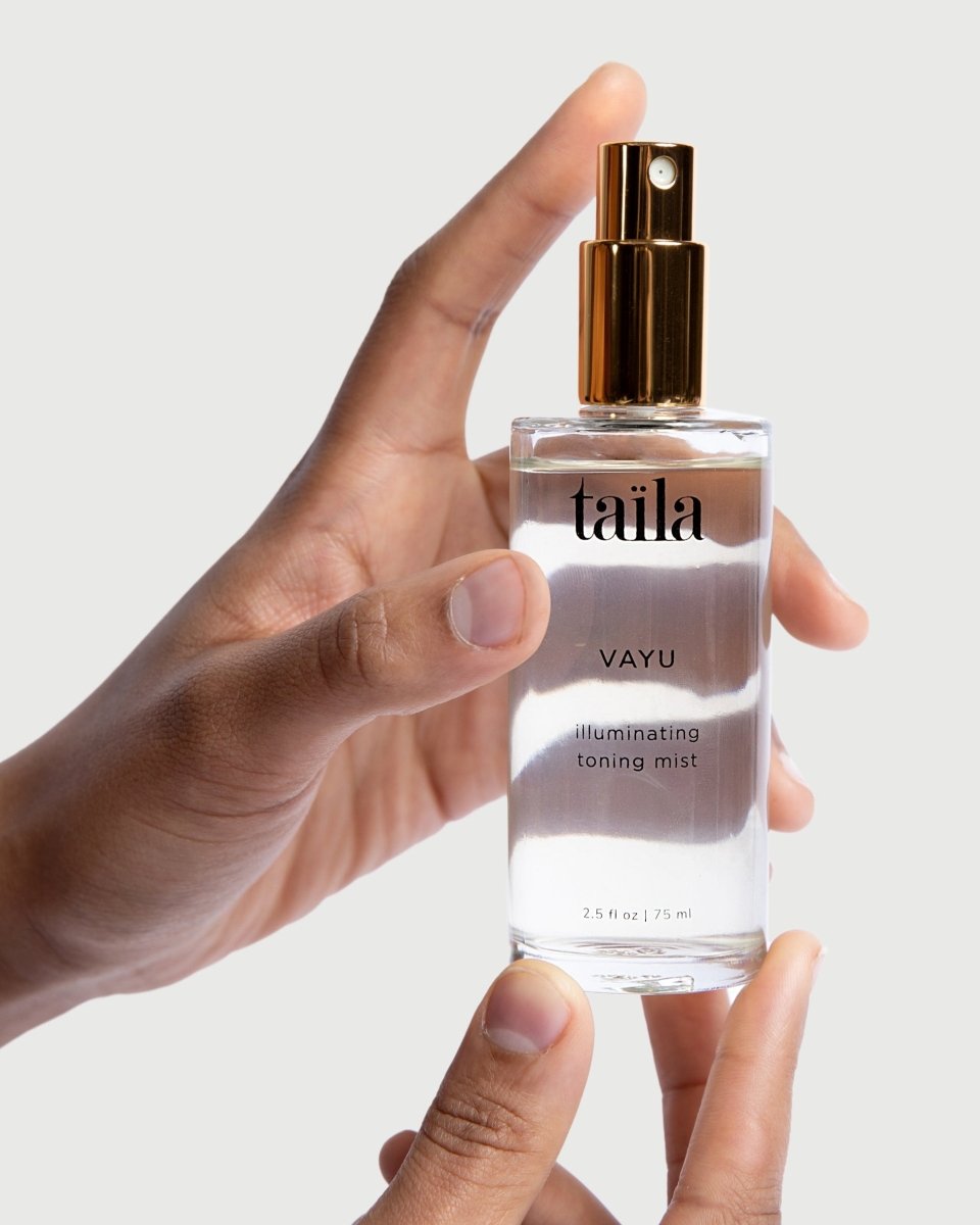 A hand gently holding the taïla Vayu Illuminating Toning Mist bottle against a clean, minimalist white background.