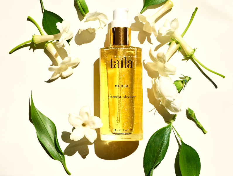 Taila ayurvedic skincare product bottle surrounded by white flowers and green leaves on a light background