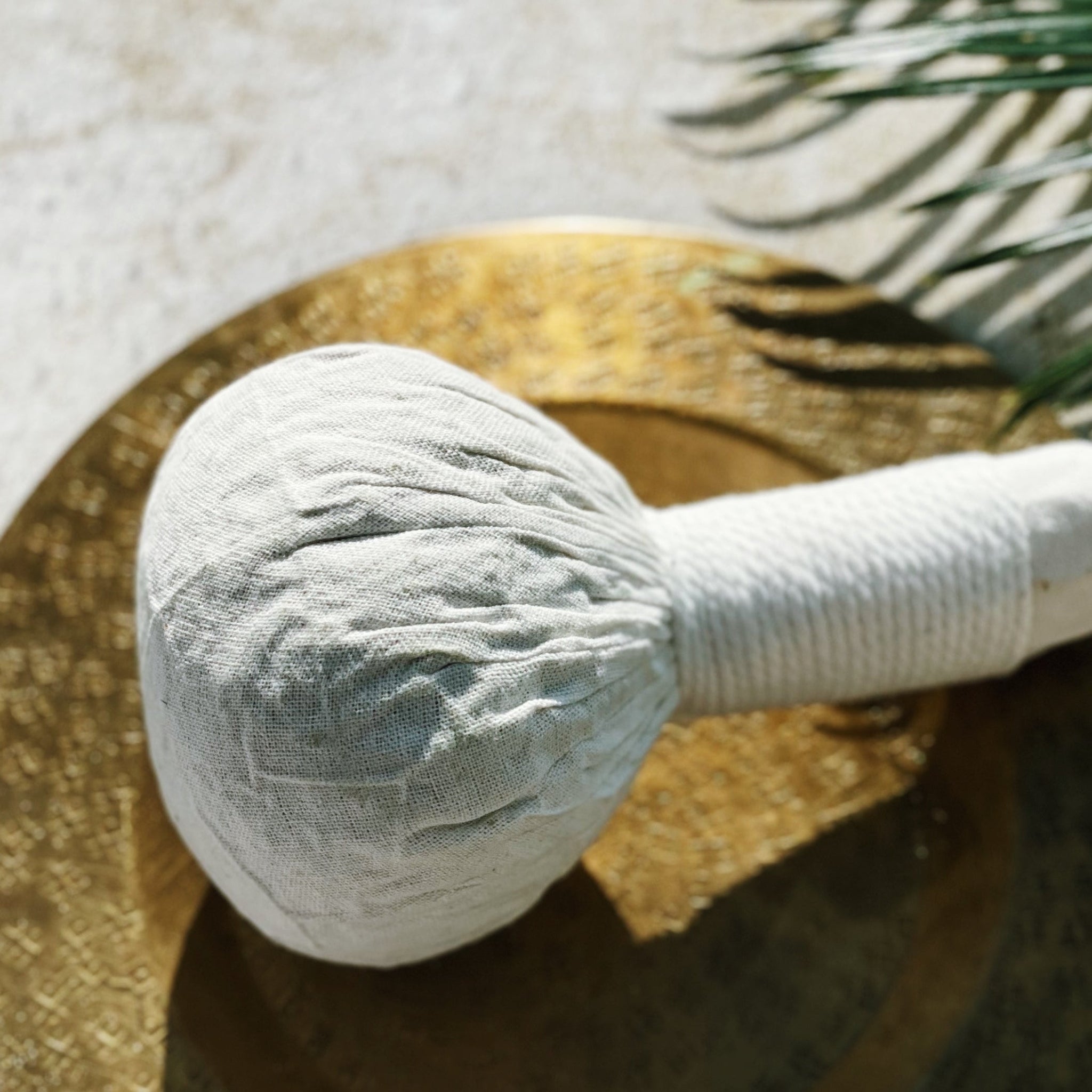 A traditional hand-tied Ayurvedic herbal poultice filled with active botanical powders and leaves, resting mindfully on a polished brass plate, illustrating our targeted and restorative skin therapies
