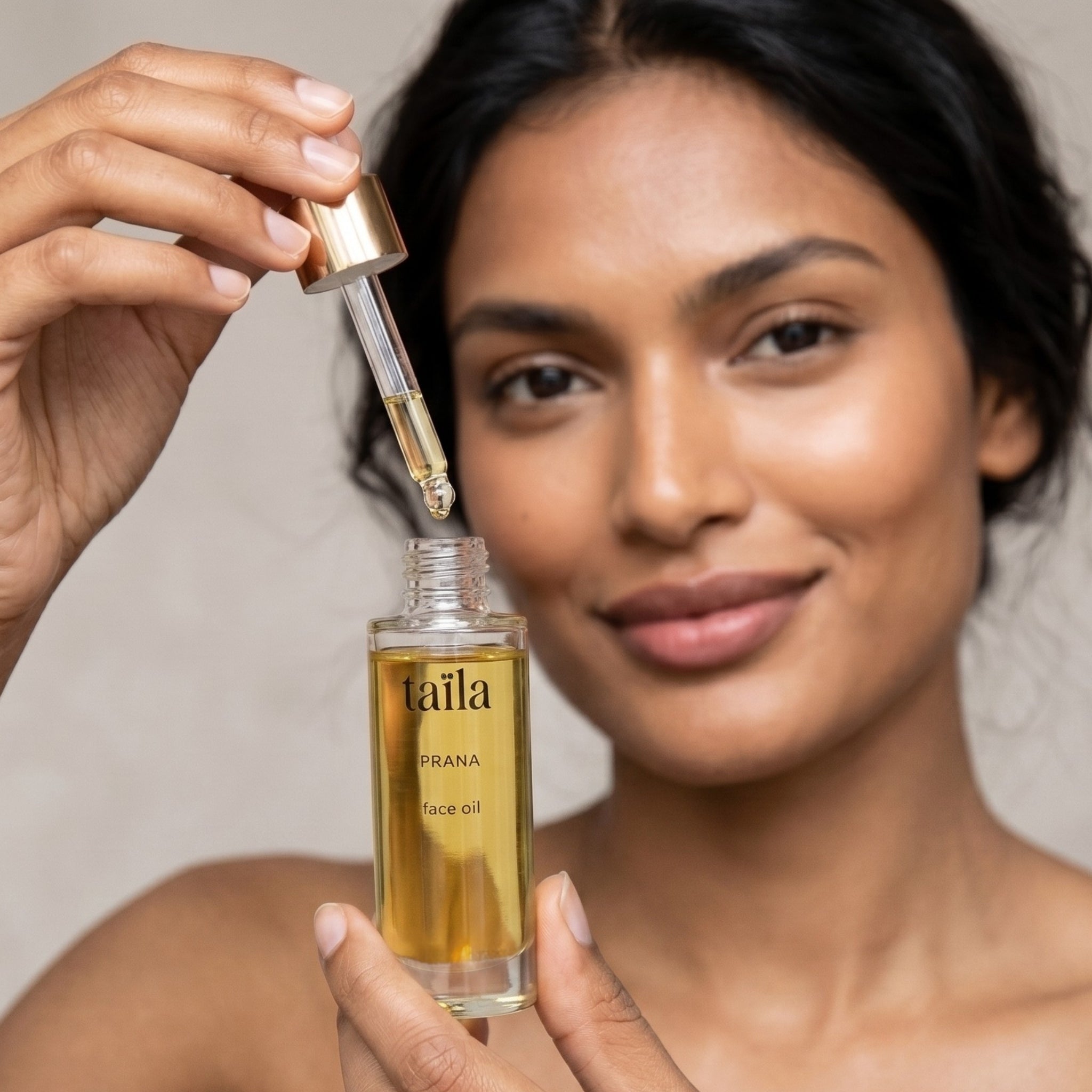 An elegant Indian woman holding the taïla PRANA Face Oil, preparing to apply the formula with a glass dropper, showcasing a luxury Ayurvedic ritual for deep cellular skin restoration.