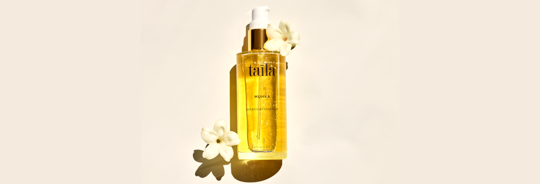 A luxury glass bottle of MUHKA Botanical Oil Cleanser nestled among fresh, delicate blossoms, illustrating the gentle, non-stripping purity of this Ayurvedic papaya and turmeric infused cleansing oil