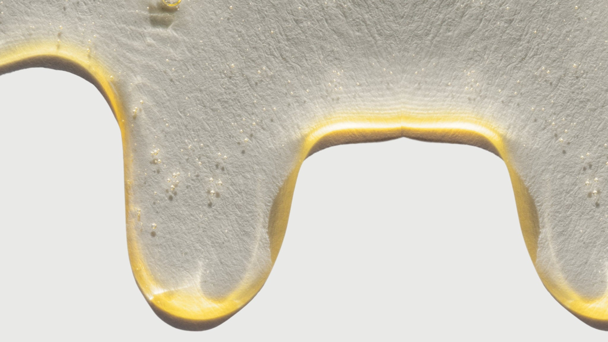 A detailed macro texture shot of taïla MUHKA Botanical Oil Cleanser, showing a rich, golden, velvety fluid with delicate oil micro-droplets, overlaid with five-star verified customer reviews.