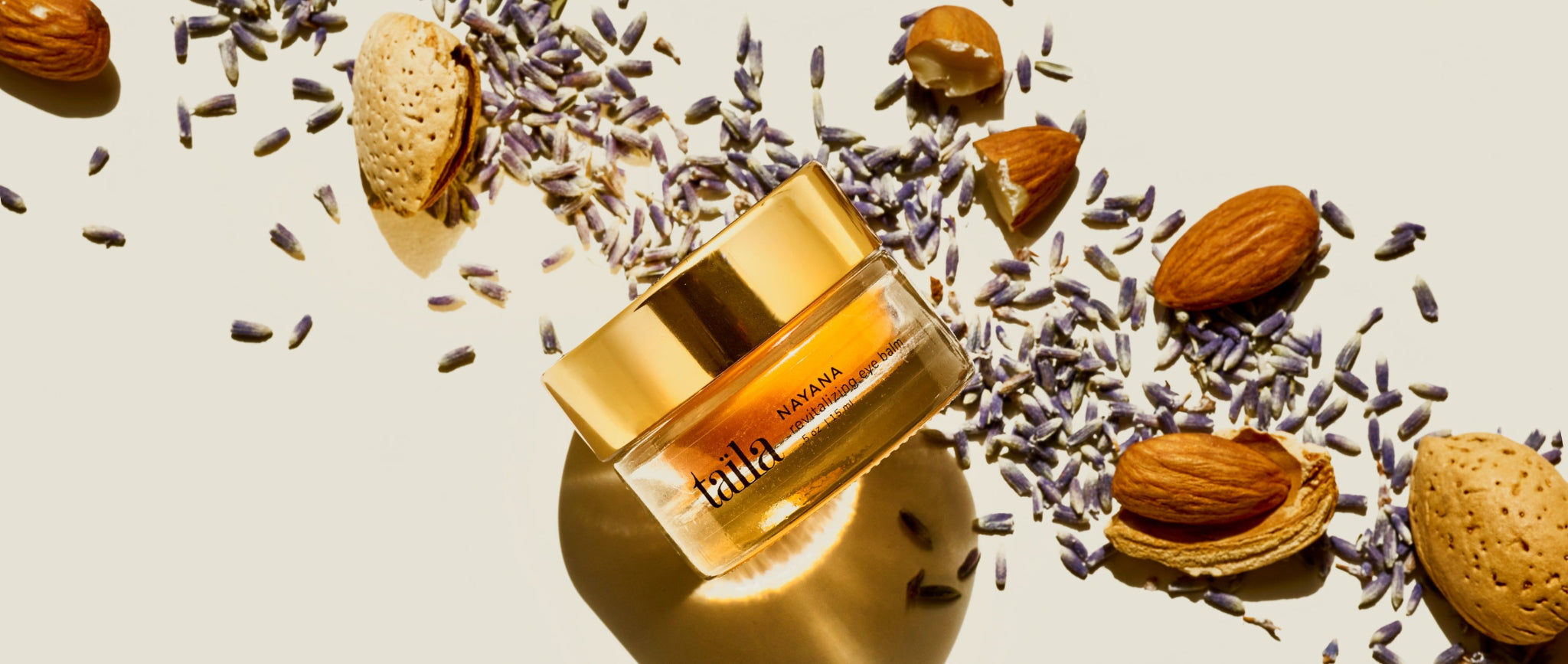 A luxurious jar of Nayana Revitalizing Eye Balm elegantly displayed alongside sweet almonds and fresh lavender blossoms, emphasizing the rich, plant-based Ayurvedic formulation.
