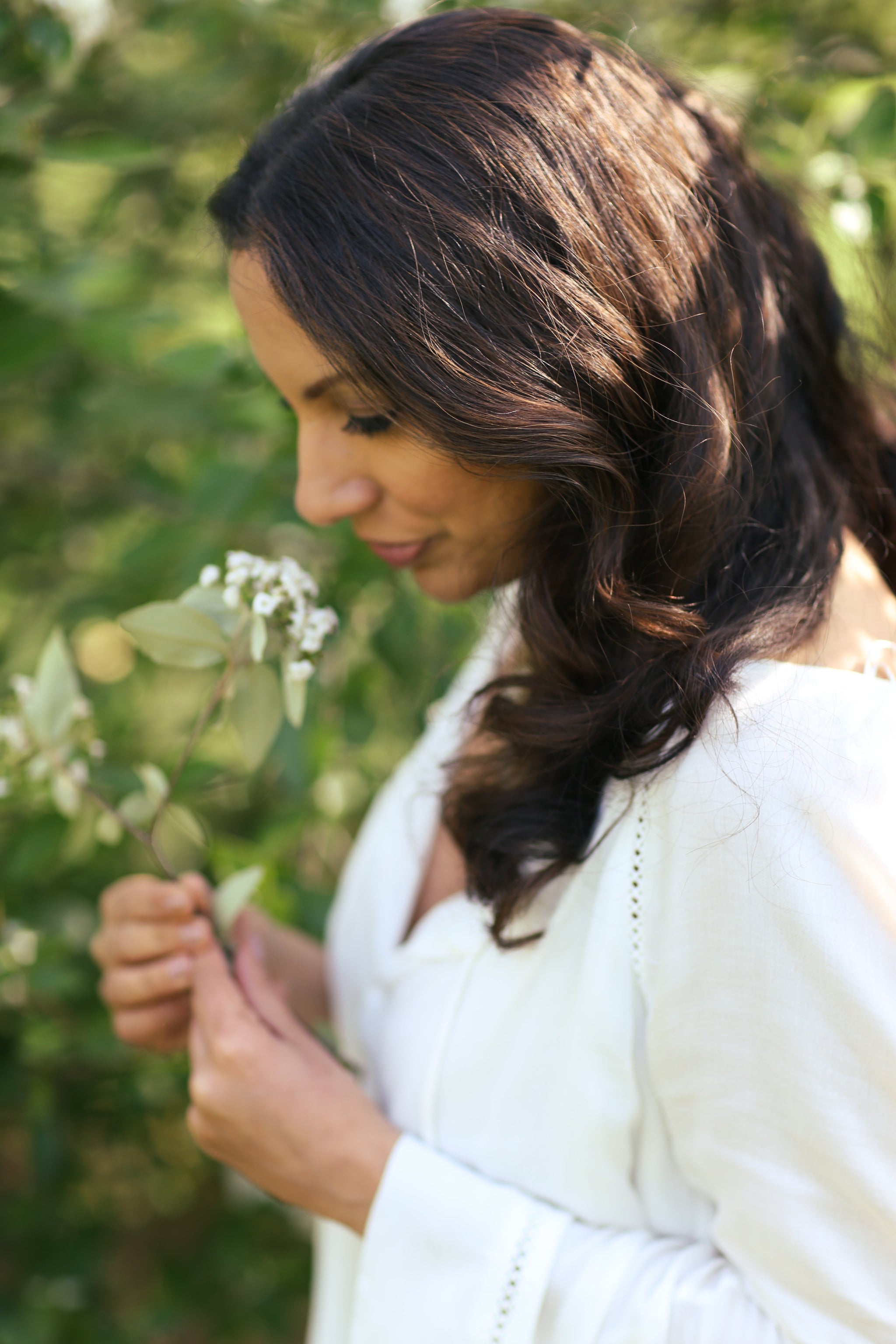Close-up portrait of Shadoh founder closing her eyes and delicately smelling fresh Kerala blossoms, illustrating her hands-on approach to sourcing raw botanical intelligence for the brand's scent profiles.