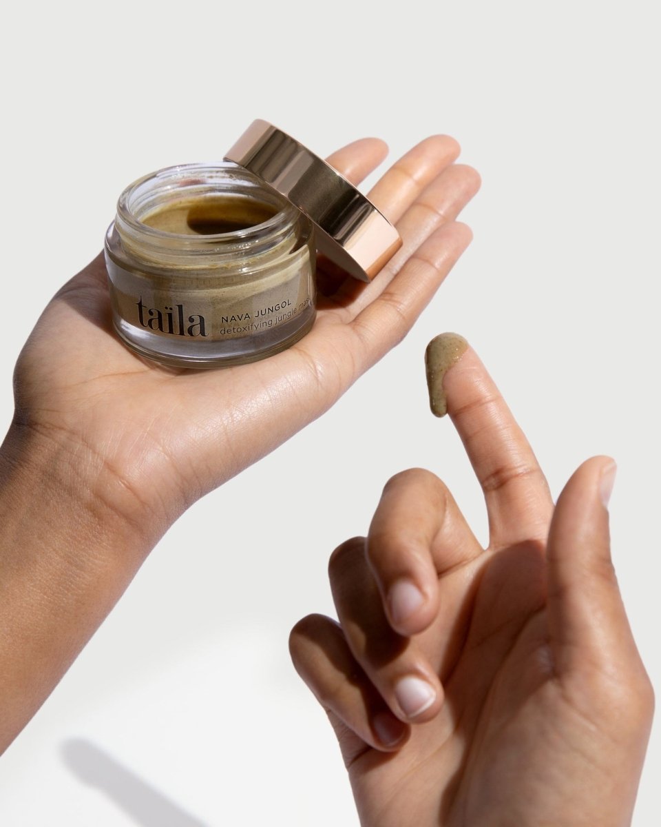 hand gently holding the taïla NAVA JUNGOL Detoxifying Jungle Face Mask bottle against a clean, minimalist white background.