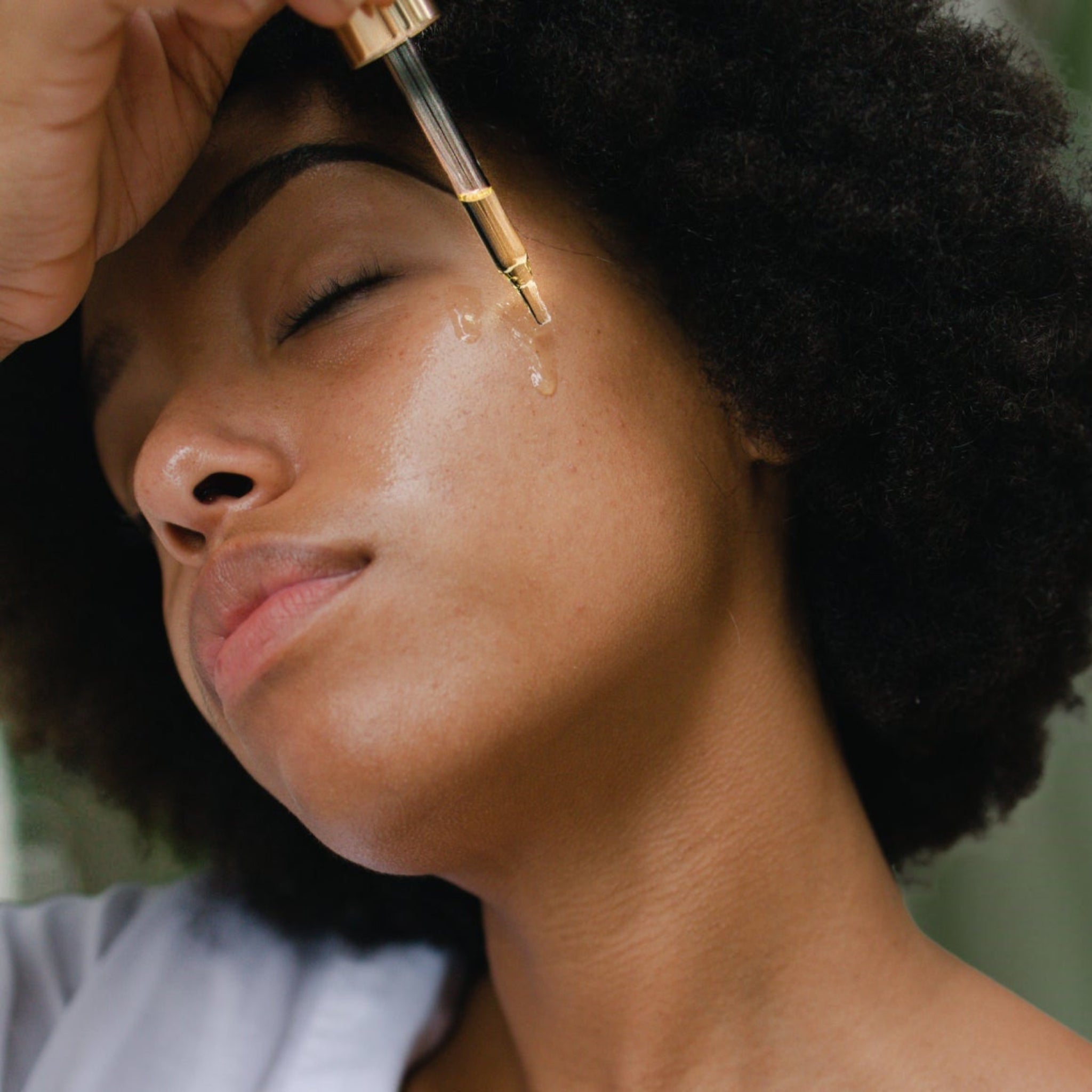 Black woman mindfully applying taïla Prana Face Oil to her cheek for a hydrated, radiant complexion.