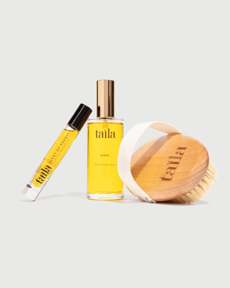 An unboxed arrangement of the taïla KAYA body oil, SCENT OF SHANTI aroma oil and dry brush on a clean white background.