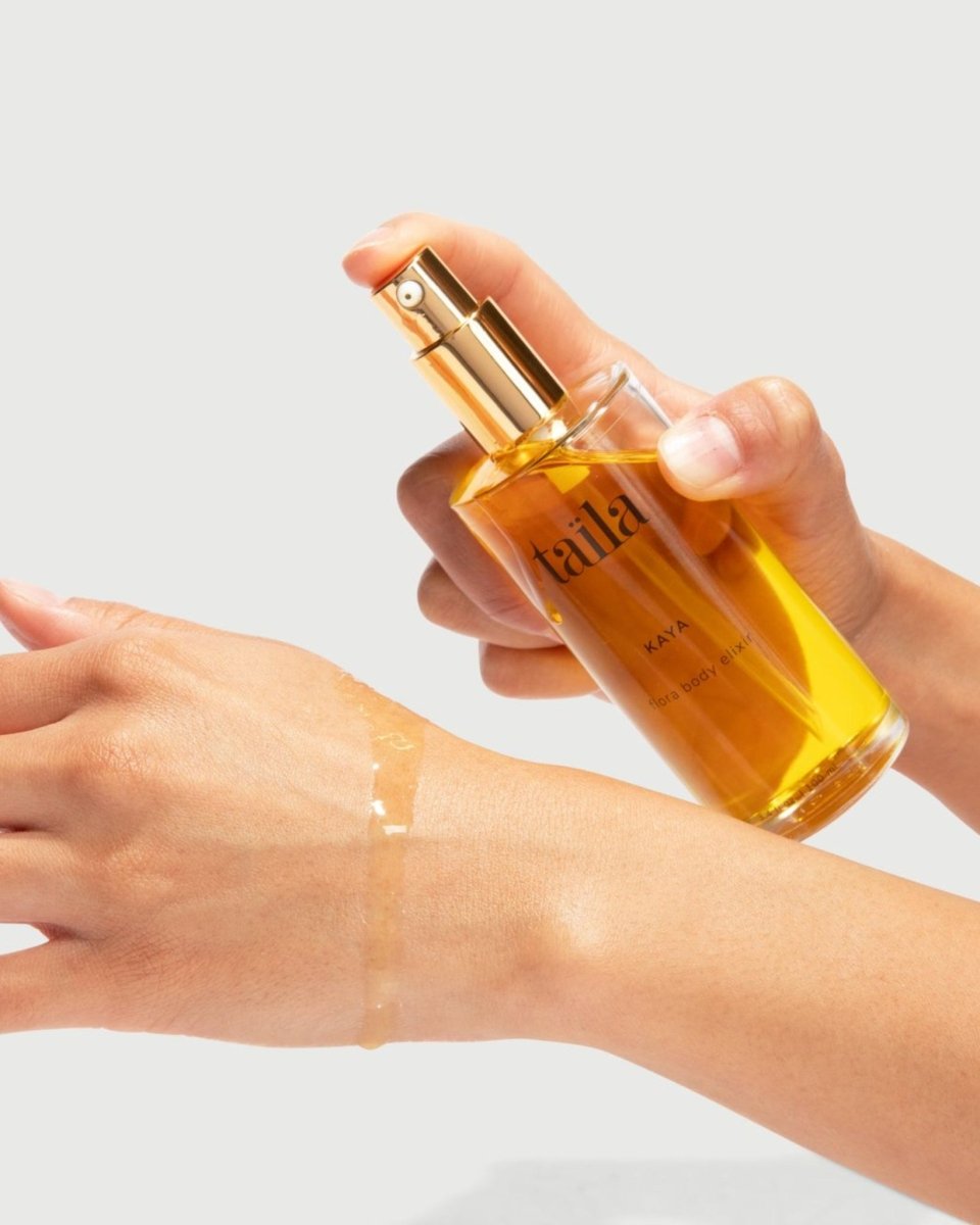 A hand holding the taïla KAYA Body Oil Elixir bottle for the SAMA Body Set box on a clean white background.