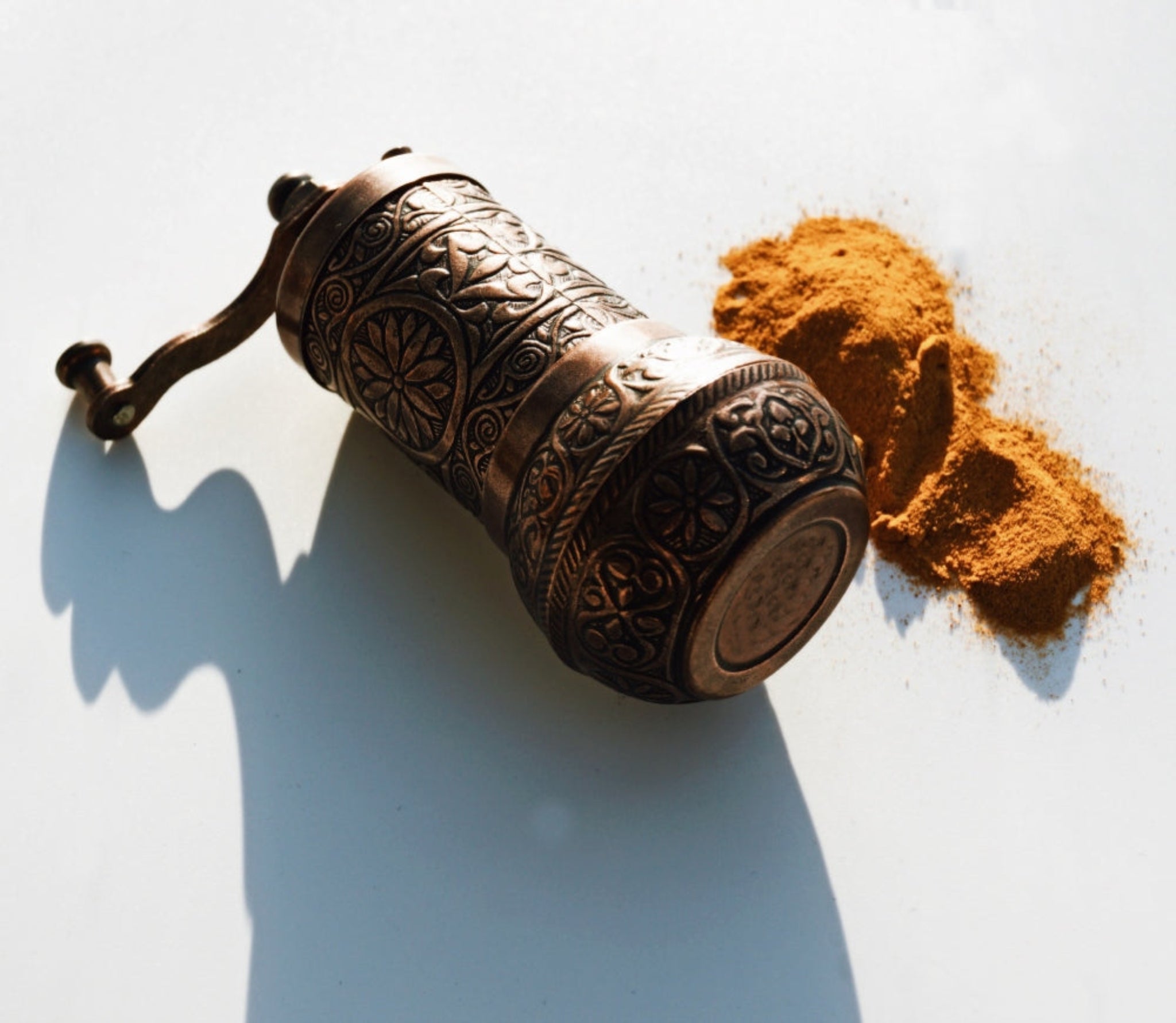 A traditional hand-carved copper grinder crushing raw, vibrant orange turmeric roots to extract pure, anti-inflammatory active botanicals for our artisanal Ayurvedic formulations.